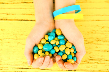 Hands with blue-yellow candies - colors of flag of Ukraine, on wooden background