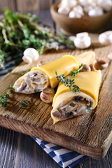 Pancakes with creamy mushrooms on wooden cutting board, closeup