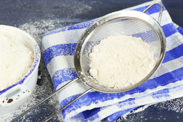 Sifting flour through sieve on wooden table, closeup