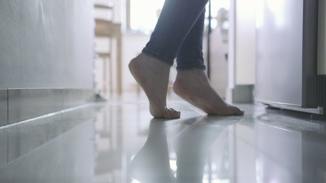 Female legs without shoes walking in the kitchen.