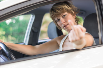 Young woman driving car and showing middle finger