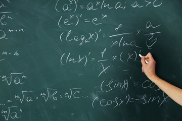 Female hand writing formulas on blackboard with chalk, close up