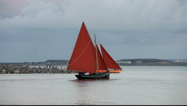 Traditional boat Galway Hooker, with red sail leaving docks