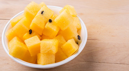 Yellow watermelon fruit in white bowl on wooden cutting board