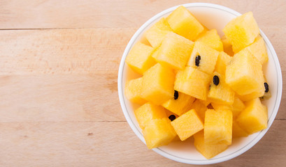 Yellow watermelon fruit in white bowl on wooden cutting board