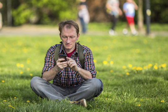 Man with smartphone sitting on the grass in a city Park.