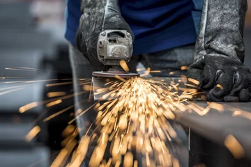 Rolgordijnen Fabrieksarbeider die metaal snijdt met veel scherpe vonken © Sasint