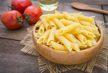 Raw penne pasta in wooden bowl