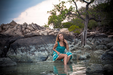 Young beautiful woman in long turquoise dress sitting on a stone