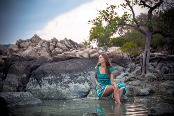 Fototapeta na wymiar Young beautiful woman in long turquoise dress sitting on a stone