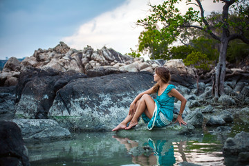 Fototapeta na wymiar Young beautiful woman in long turquoise dress sitting on a stone