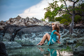 Young beautiful woman in long turquoise dress sitting on a stone