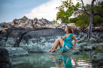 Young beautiful woman in long turquoise dress sitting on a stone