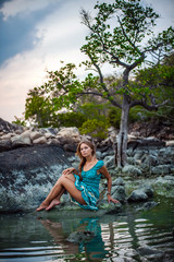 Fototapeta premium Young beautiful woman in long turquoise dress sitting on a stone