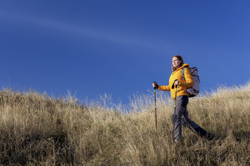 Female hiker ascents the grassy hill using trekking poles