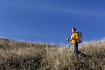 Naklejka na ściany i meble Female hiker walks downhill and enjoys warm sunlight