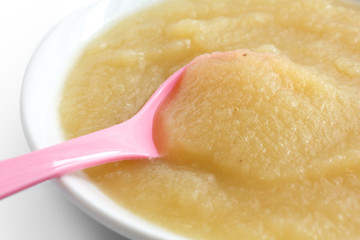White dish of apple sauce with pink baby spoon.