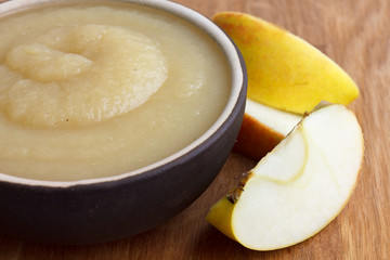 Apple sauce in rustic brown dish on dark wood. Sliced apples.
