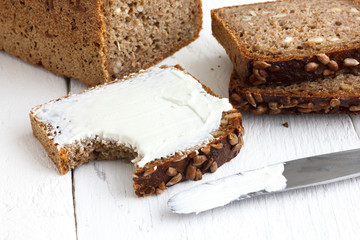 Sunflower seed loaf sliced, cream spread, knife.