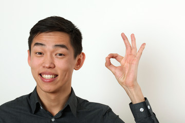 Smiling young Asian man giving the okay sign and looking at came