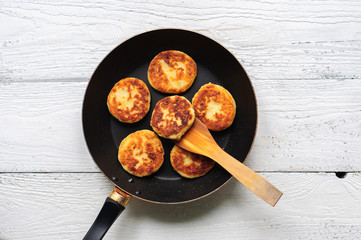 Cottage cheese pancakes in frying pan on wooden background