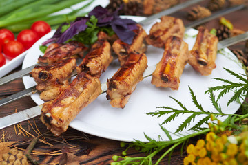 Three skewers with grilled ribs lie on a white plate with cherry