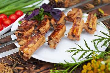 Three skewers with grilled ribs lie on a white plate with cherry