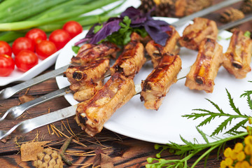 Three skewers with grilled ribs lie on a white plate with cherry