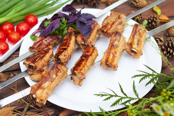 Three skewers with grilled ribs lie on a white plate with cherry