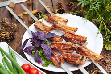 Three skewers with grilled ribs lie on a white plate with cherry
