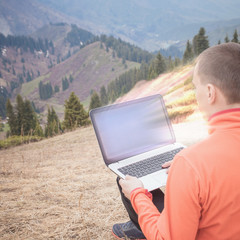 man uses laptop remotely at mountain