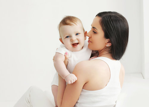 Portrait of smiling baby with mother at home in white room