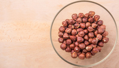 Hazelnuts in a glass bowl on wooden cutting board