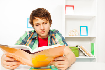 Clever boy read book sitting by table do homework