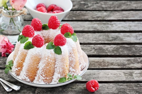 Vanilla bundt cake with raspberries on a rustic dark background