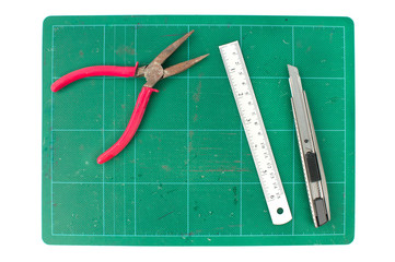 Green cutting mats with iron ruler pliers and cuter on white bac