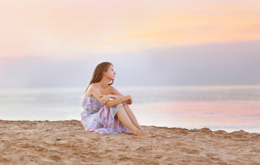 Young woman sitting on the beach at coast enjoying sea sunset