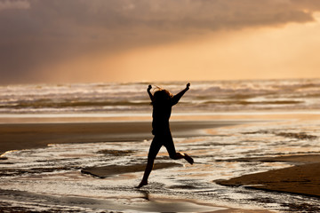Girl at sunset jumps into water.