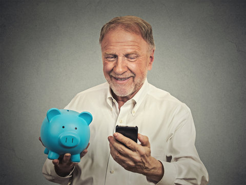 happy senior man holding piggy bank looking at smart phone