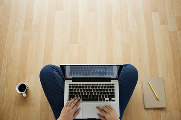 girl sitting on a wooden floor laptop coffee cup and notebook