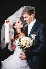 Bride And Groom Kissing Under Veil Holding Flower Bouquet In