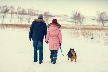 Young couple with dog walking in the snowy field 