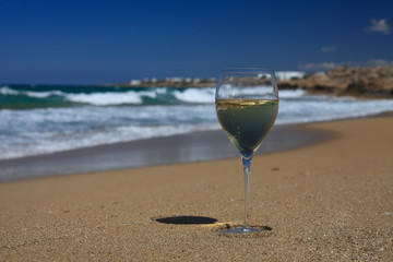 glass of white wine on the seashore against a blue sky.
