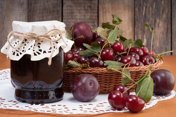 The jar of homemade fruits jam with plums and cherries in basket