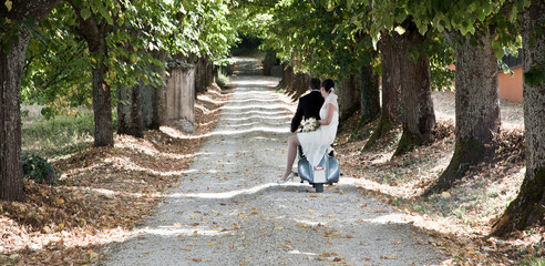 Coppia di sposi su moto italiana lungo un viale alberato