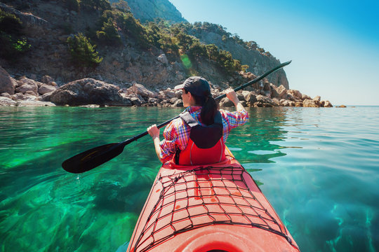 Woman kayaking at sea along rocky shore of island. Traveling