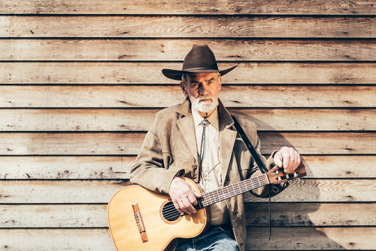Middle Age Guitarist Leaning on Wooden House Wall