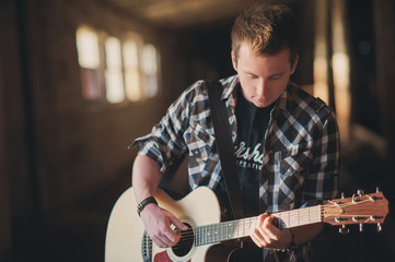 A young man stands with a guitar in hand lit by sunlight