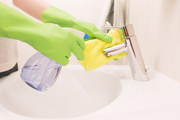 Woman doing chores in bathroom, cleaning sink and faucet with sp