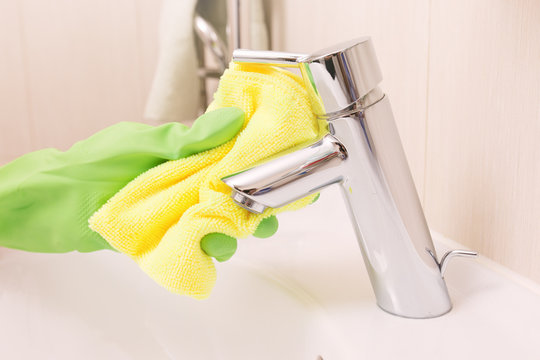 Woman doing chores in bathroom, cleaning sink and faucet with sp